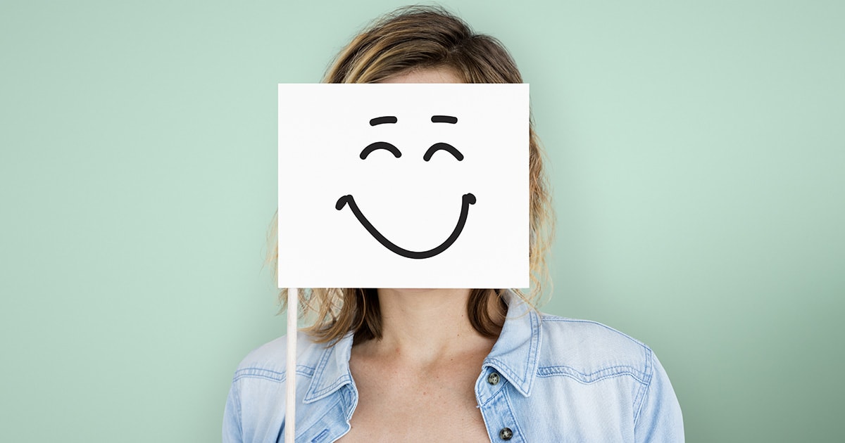 Egy nő maga elé tart egy mosoly táblát, de valójában mögötte szomorú és lelki problémákkal küzd, de kifele azt tükrözi, hogy boldog és minden rendben.