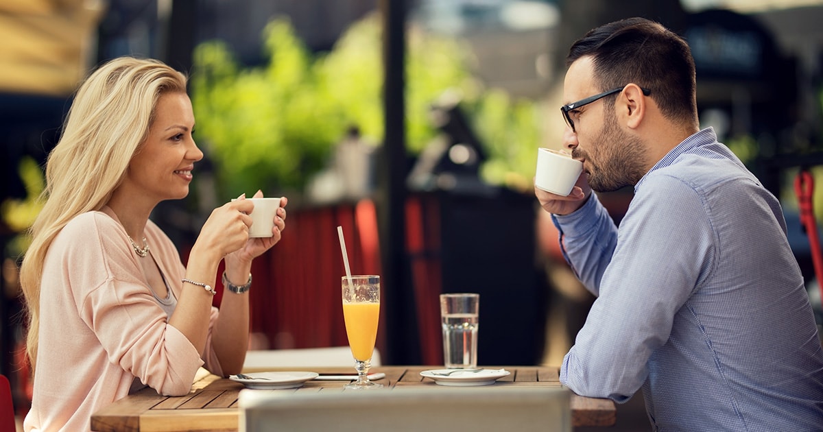 Első randi egy kávézóban, egy férfi és egy nő egymással szemben ül és mosolyogva beszélgetnek