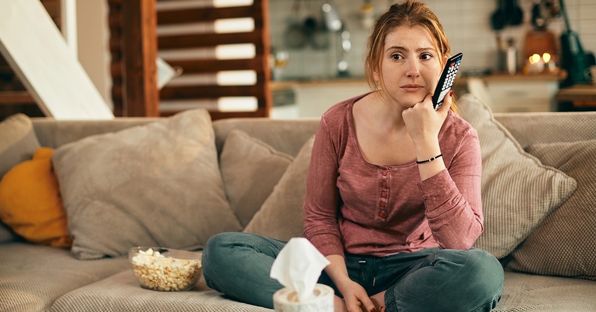 Egy nő egyedül ül a kanapén és azon gondolkodik szomorúan, hogy nincs kivel beszéljen, támogató beszélgetőtársa lenne szüksége.