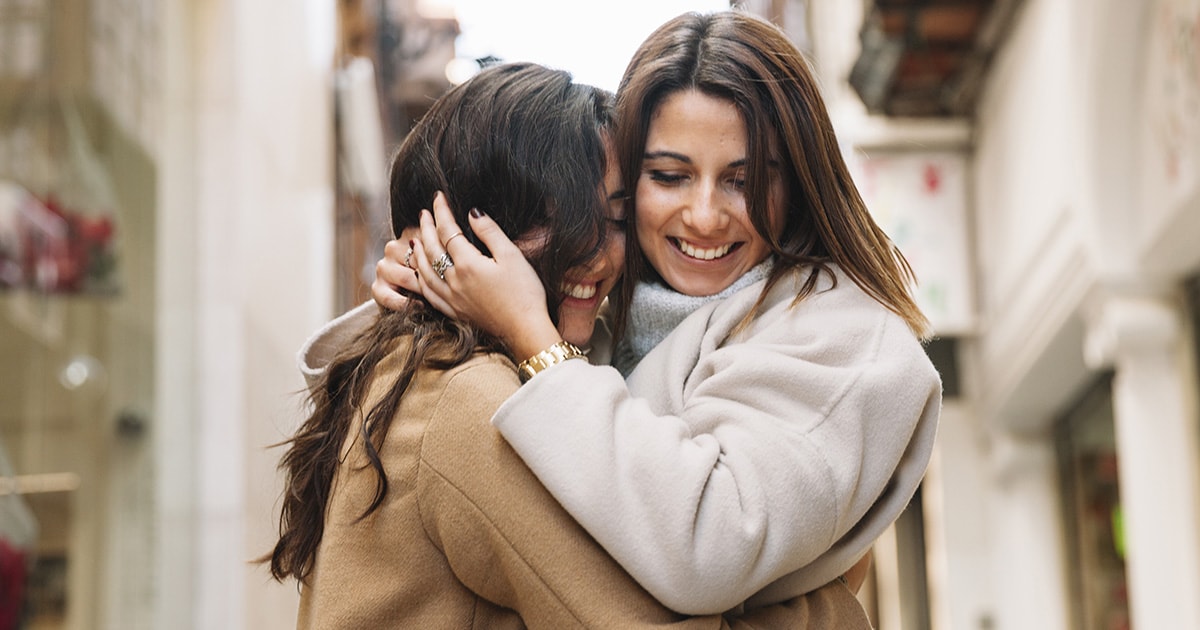 Két barátnő boldogan átöleli egymást szorosan az utcán