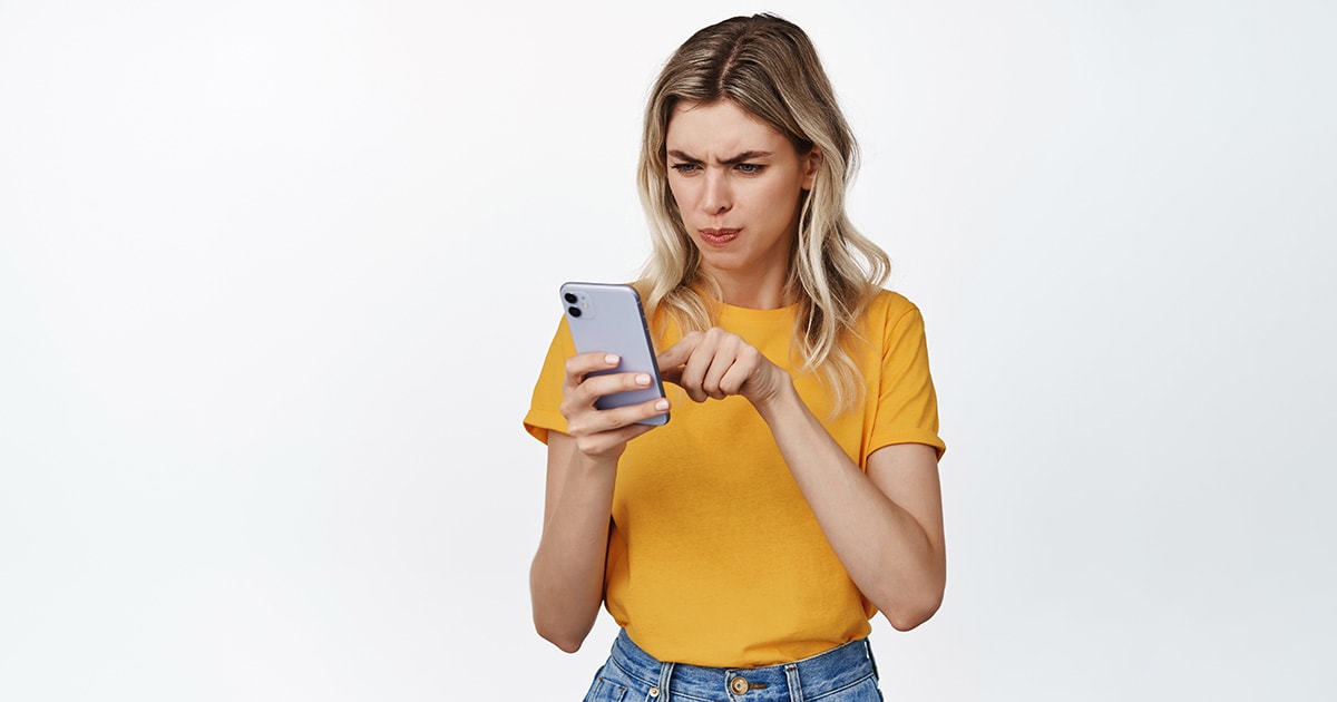 Egy ideges nő, aki a telefonját szorítja és megnyomja a tiltás gombot a Facebookon és a többi közösségi felületen